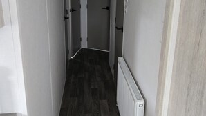 A narrow hallway with wooden flooring, white walls, and a white radiator on the right.