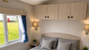 A bedroom with a bed, bedside tables, a window with curtains, and a view of the outdoors.
