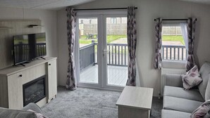 A living room with a sofa, a TV on a cabinet, a fireplace, and a balcony with curtains.
