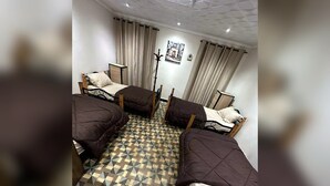 A room with four beds arranged in a square, a patterned floor, and a coat rack. - Casbah Hostel (Algiers)