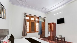 Une chambre d’hôtel avec un lit, une petite table avec une bouilloire, une armoire, un téléviseur et une fenêtre avec des rideaux.