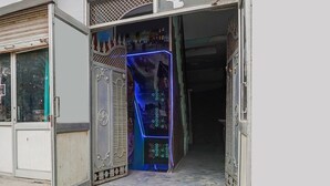 Une entrée d’immeuble agrémentée d’un portail en métal décoratif, d’une petite pelouse et d’une structure illuminée de lumière bleue à l’intérieur.