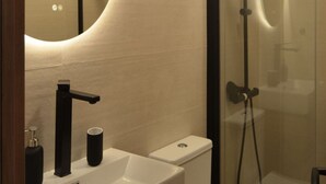 Une salle de bain moderne avec un miroir incurvé, un robinet noir, un lavabo blanc et une douche à parois de verre.