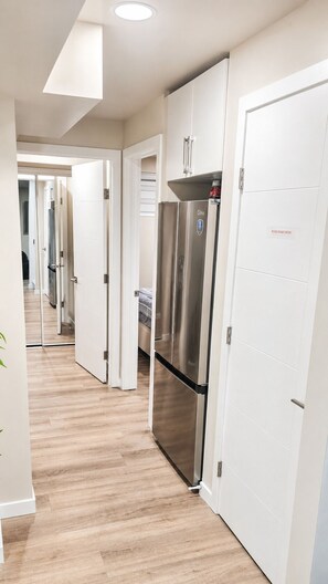 A hallway with a stainless steel refrigerator, white doors, and a wooden floor. - Your Devonshire, Transcona Retreat | Cozy 2BR Haven (Winnipeg)