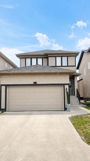 A two-story house with a garage, a staircase, and a potted plant. - Your Devonshire, Transcona Retreat | Cozy 2BR Haven (Winnipeg)