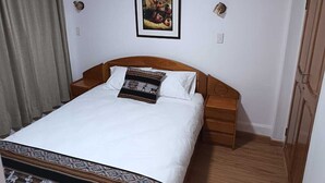 A bedroom with a bed, a nightstand, a wooden wardrobe, a framed picture on the wall, and a curtain. - Omaya House: A Cozy and Quiet Room for Your Stay in Downtown Cusco (Cusco)