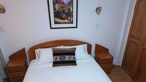 A neatly made bed with white linens and patterned pillows, wooden headboard, two bedside tables, and a wooden wardrobe. - Omaya House: A Cozy and Quiet Room for Your Stay in Downtown Cusco (Cusco)