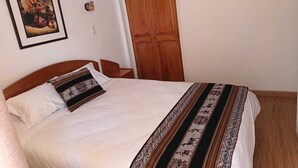 A bedroom with a bed, a wooden wardrobe, a framed picture on the wall, and a light switch. - Omaya House: A Cozy and Quiet Room for Your Stay in Downtown Cusco (Cusco)