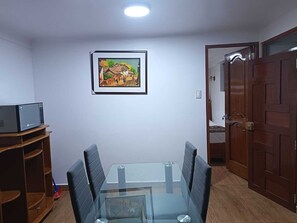 A dining area with a glass table, black chairs, a framed painting, a television on a wooden stand, and a wooden door. - Omaya House: Your Ideal Family-Friendly Mini-Apartment Retreat (Cusco)