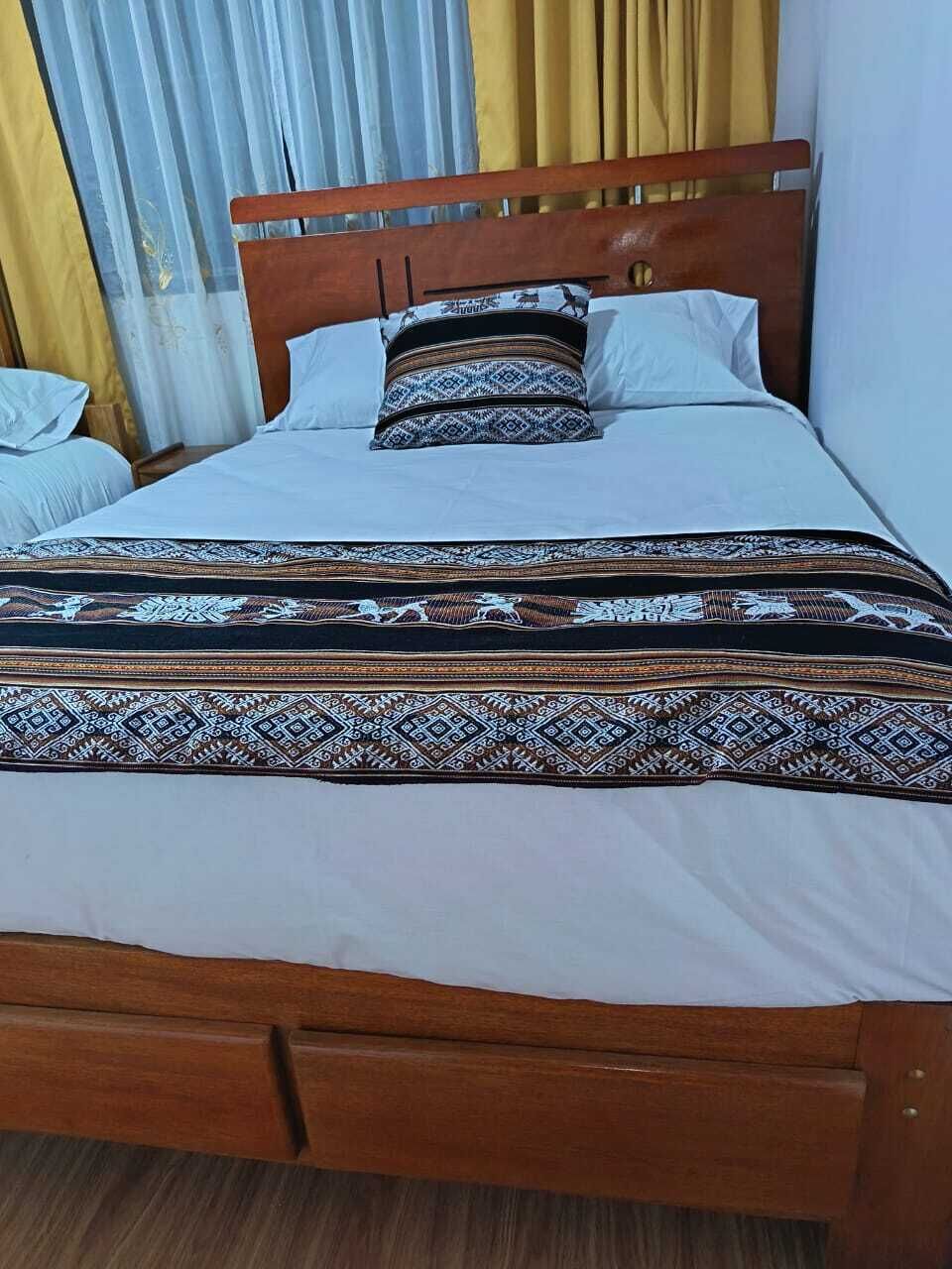 A bed with a wooden headboard, white bedding, and patterned bedspread.