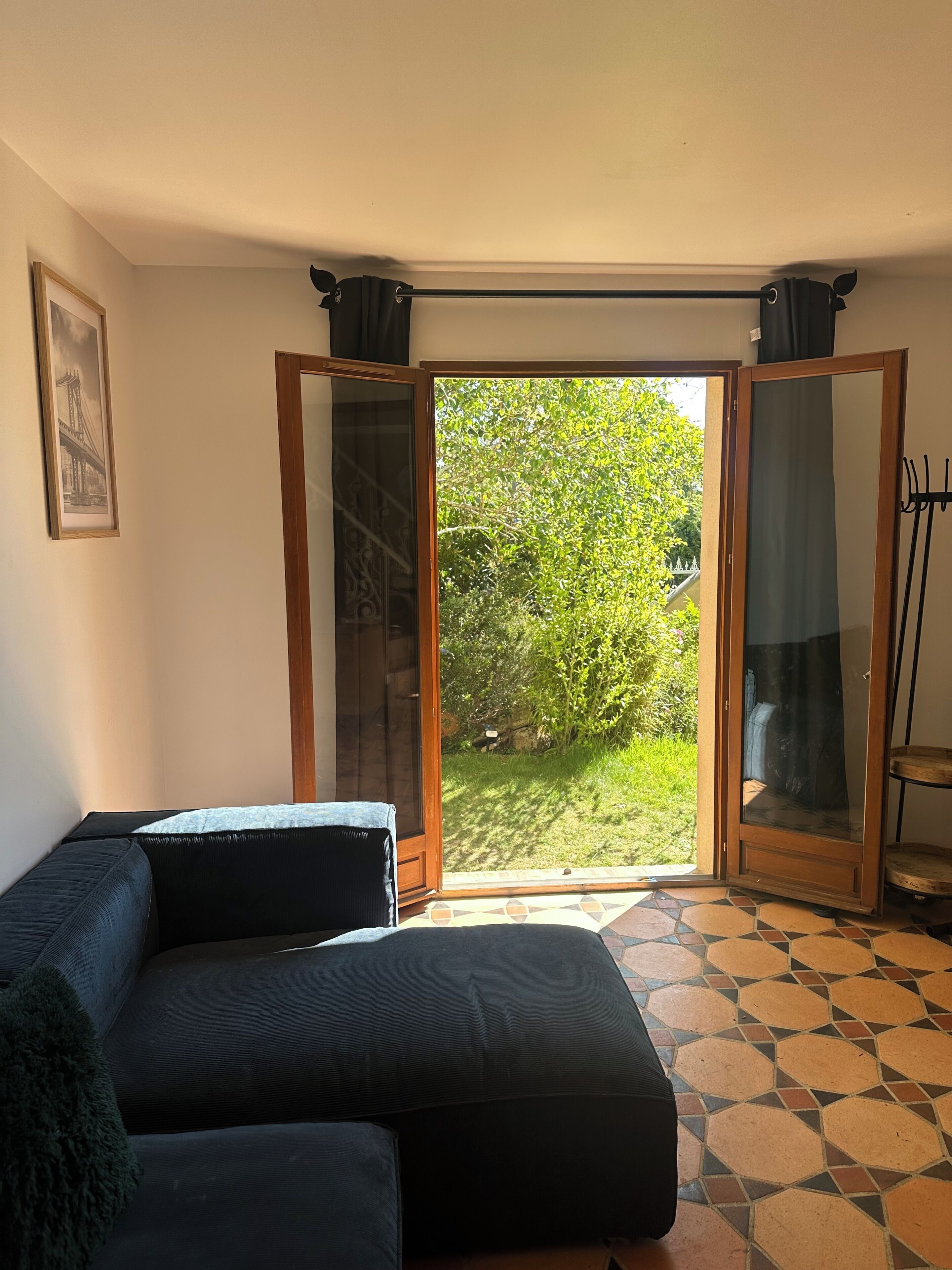 Une pièce avec un canapé, une porte donnant sur un jardin et un tableau encadré au mur.
