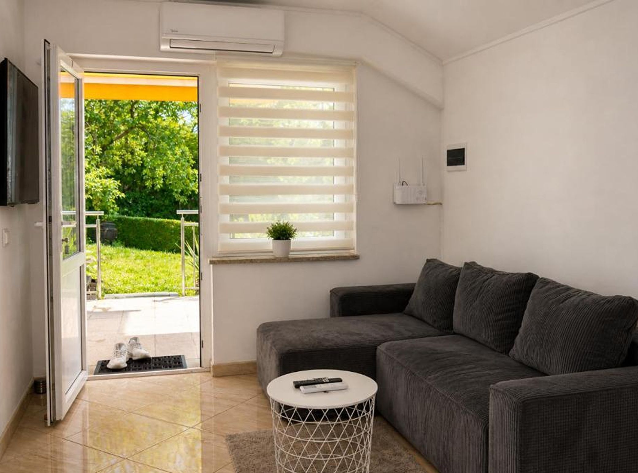 Un soggiorno moderno con un divano grigio, un tavolino rotondo e una porta vetrata scorrevole che dà su un balcone.