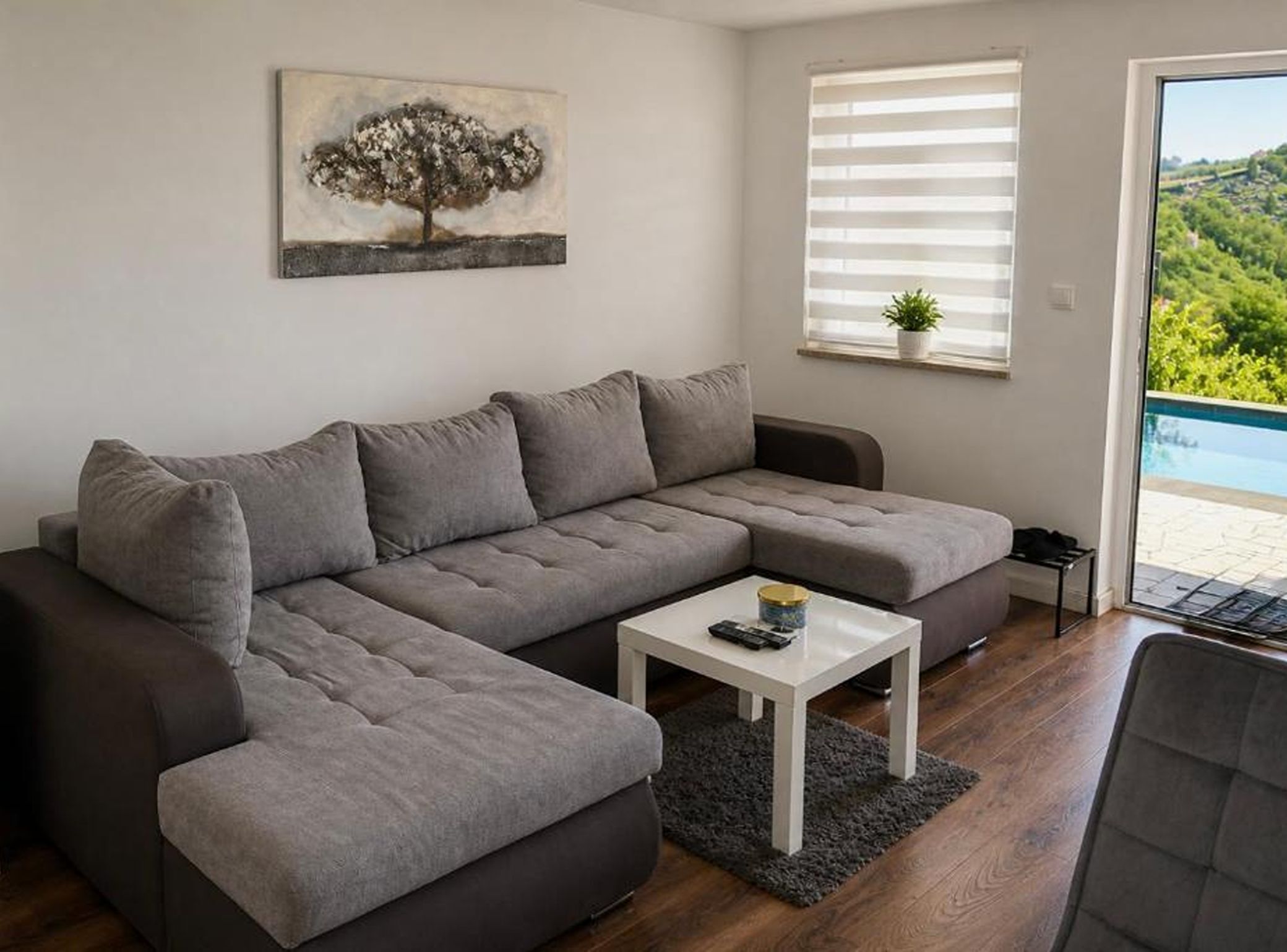 A modern living room with a grey sectional sofa, a small white coffee table, and a painting of a tree.