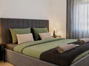 Una cama bien hecha con una colcha verde y negra, dos almohadas y toallas enrolladas.