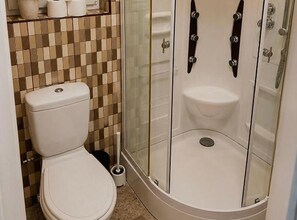 Un baño con inodoro, cabina de ducha y pared con azulejos.