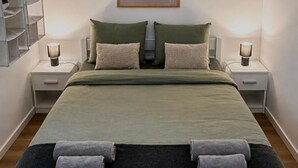 A neatly made bed with a green bedspread, two pillows, and two rolled towels. There are two bedside tables with lamps. - Holiday Home Damian (Zagreb)