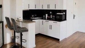 A compact kitchen with white cabinets, a black countertop, and a small bar area with two stools. - Holiday Home Damian (Zagreb)