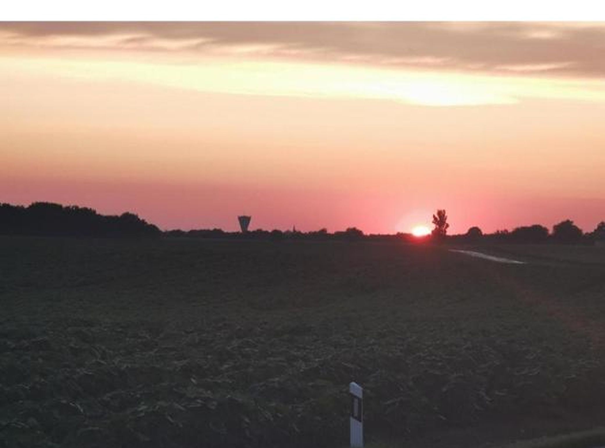Un atardecer sobre un paisaje llano con una carretera y una estructura distante.