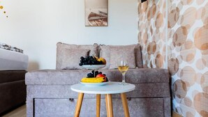 A modern living room with a grey sofa, a small round table with fruit and a glass of wine, and a patterned wall.