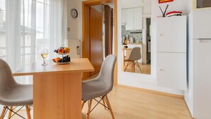 A modern kitchen with white cabinets, a wooden dining table with two chairs, and a fruit bowl on the table.