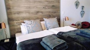 Habitación de hotel con cabecera de madera, dos camas con ropa de cama azul y blanca, y almohadas decorativas.