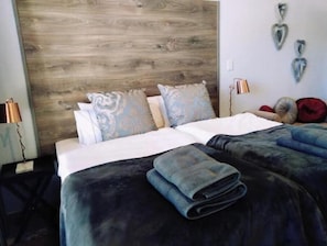 A hotel room with a wooden headboard, two beds with blue and white bedding, and decorative pillows.