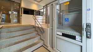Ein Hotel Eingang mit einer Rampe, die zu einem Aufzug, einer Treppe und einem rollstuhlgerechten Fahrstuhl führt.