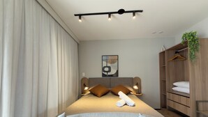 Ein modernes Schlafzimmer mit Bett, Nachttischlampen, einem Kopfteil, einem Kleiderschrank und einer hängenden Pflanze.