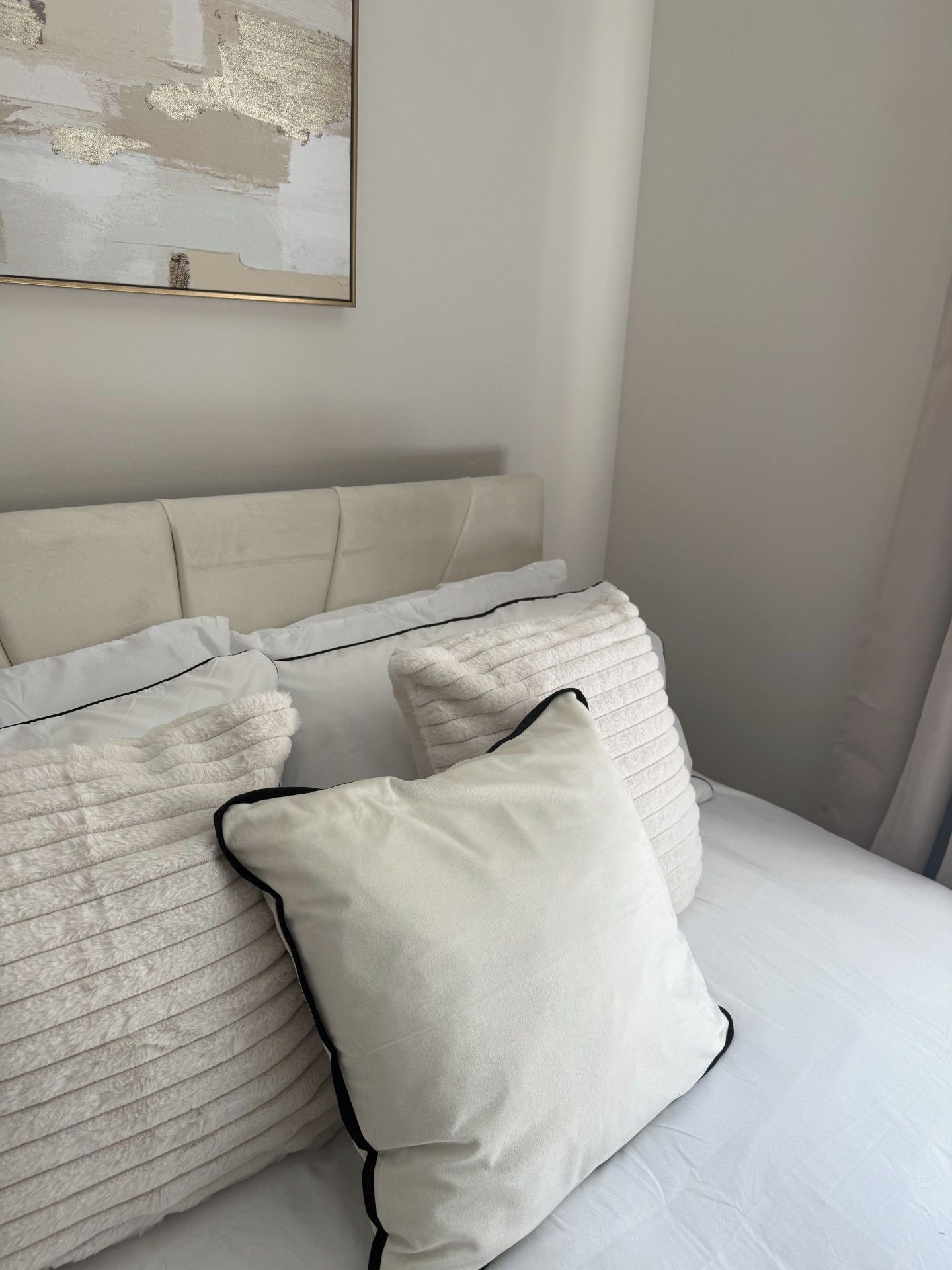 Ein Bett mit weißer Bettwäsche und mehreren Kissen, eine schlichte Wand und ein abstraktes Kunstwerk.