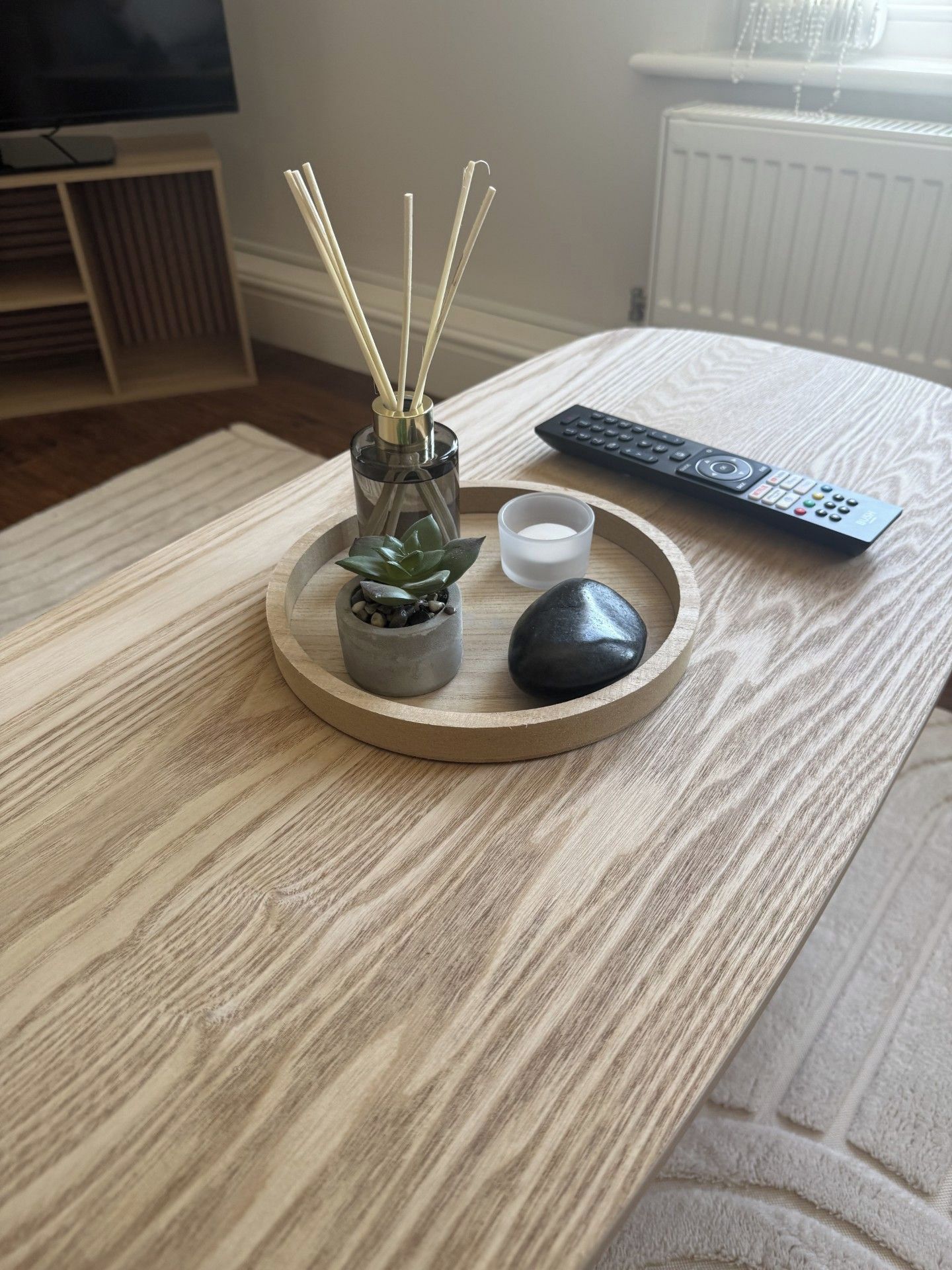Un plateau en bois sur lequel se trouvent une petite plante en pot, une bougie et une télécommande.