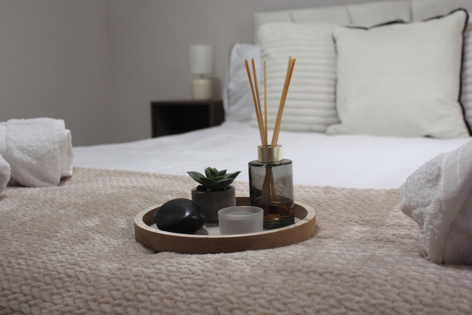 Un plateau bien organisé, sur lequel on trouve une bougie, une petite plante et des diffuseurs à bâtonnets, le tout posé sur une couverture à texture intéressante.