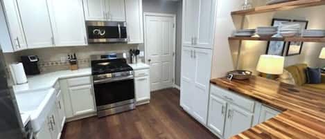 Una cocina con armarios blancos, encimera de madera, electrodomésticos de acero inoxidable y salpicadero de azulejos.
