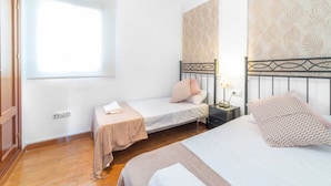 A bedroom with two single beds, a nightstand with a lamp, a window, and a wall with a leaf pattern. - Stay Near Feria, Madrid (Seville)