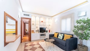 A modern living room with a checkered floor, a sofa with cushions, a television, and a plant. - Stay Near Feria, Madrid (Seville)