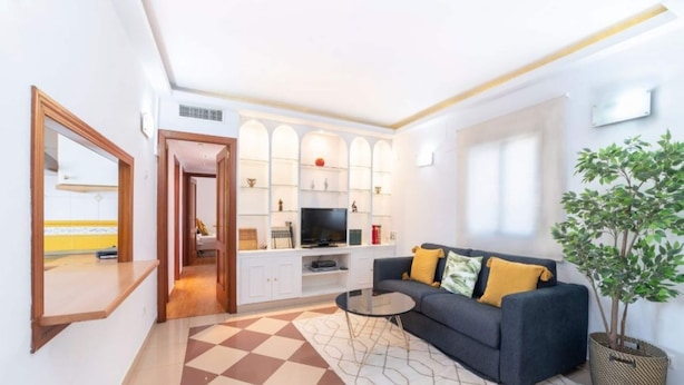 A modern living room with a checkered floor, a sofa with cushions, a TV, and a plant. - Stay Near Feria, Madrid (Seville)