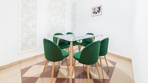 A dining area with a glass table and green chairs, white walls, and patterned wallpaper. - Stay Near Feria, Madrid (Seville)