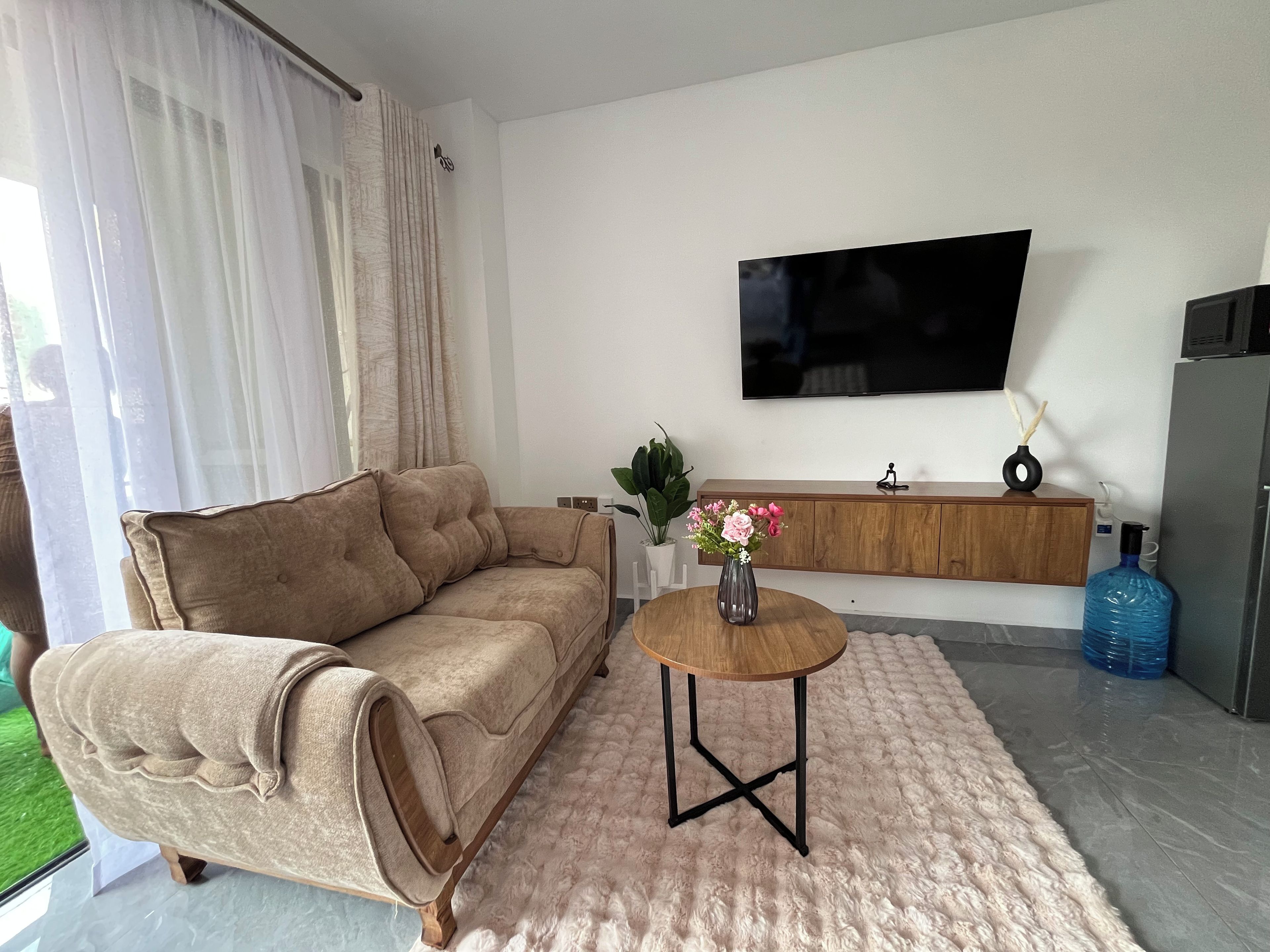 A modern living room with a beige sofa, a round coffee table, and a flat-screen TV mounted on the wall.