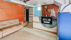 Un'area reception di un hotel con un divano, una scrivania della reception, una ventola a soffitto e una statua.