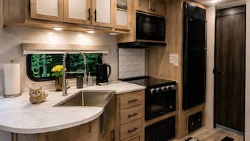 Une cuisine compacte avec des meubles en bois, un évier en acier inoxydable, une cuisinière noire et un four à micro-ondes.