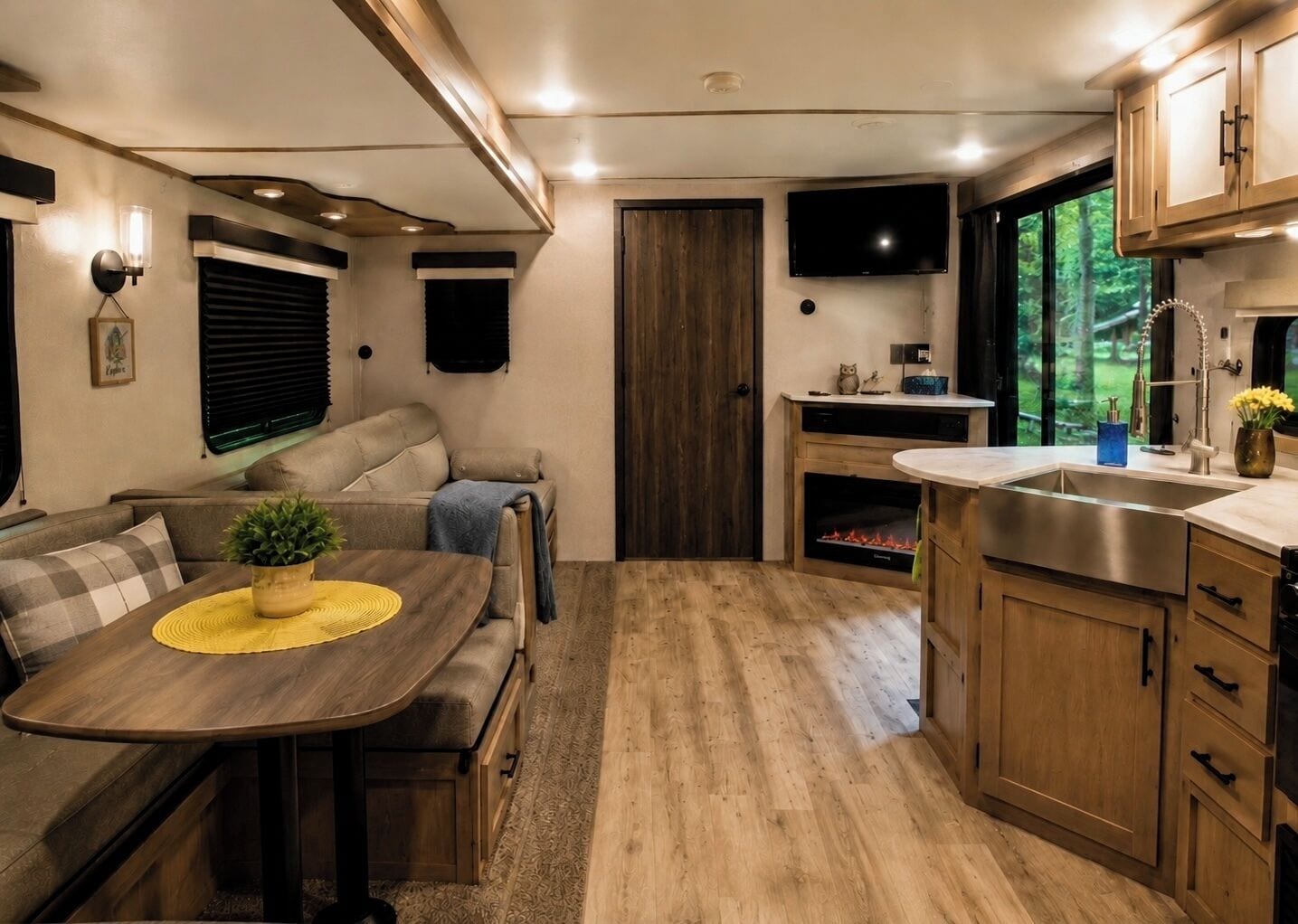 Un intérieur de camping-car compact comprenant un coin cuisine, un espace repas, un coin salon et un téléviseur fixé au-dessus de la cheminée.