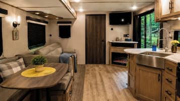 Un intérieur de camping-car compact comprenant un coin cuisine, un espace repas, un coin salon et un téléviseur fixé au-dessus de la cheminée.