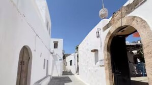Une rue étroite bordée de bâtiments blancs, avec une arche en pierre et un luminaire suspendu.