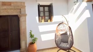 Une terrasse avec un fauteuil suspendu, un pot de fleurs et une fenêtre avec des volets.