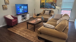 Ett vardagsrum med en platt-TV, en soffa, en röd fåtölj, ett soffbord och en gitarr.