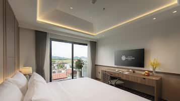 A hotel room with a large bed, a desk with a flat-screen TV, a view of the outdoors, and a balcony.