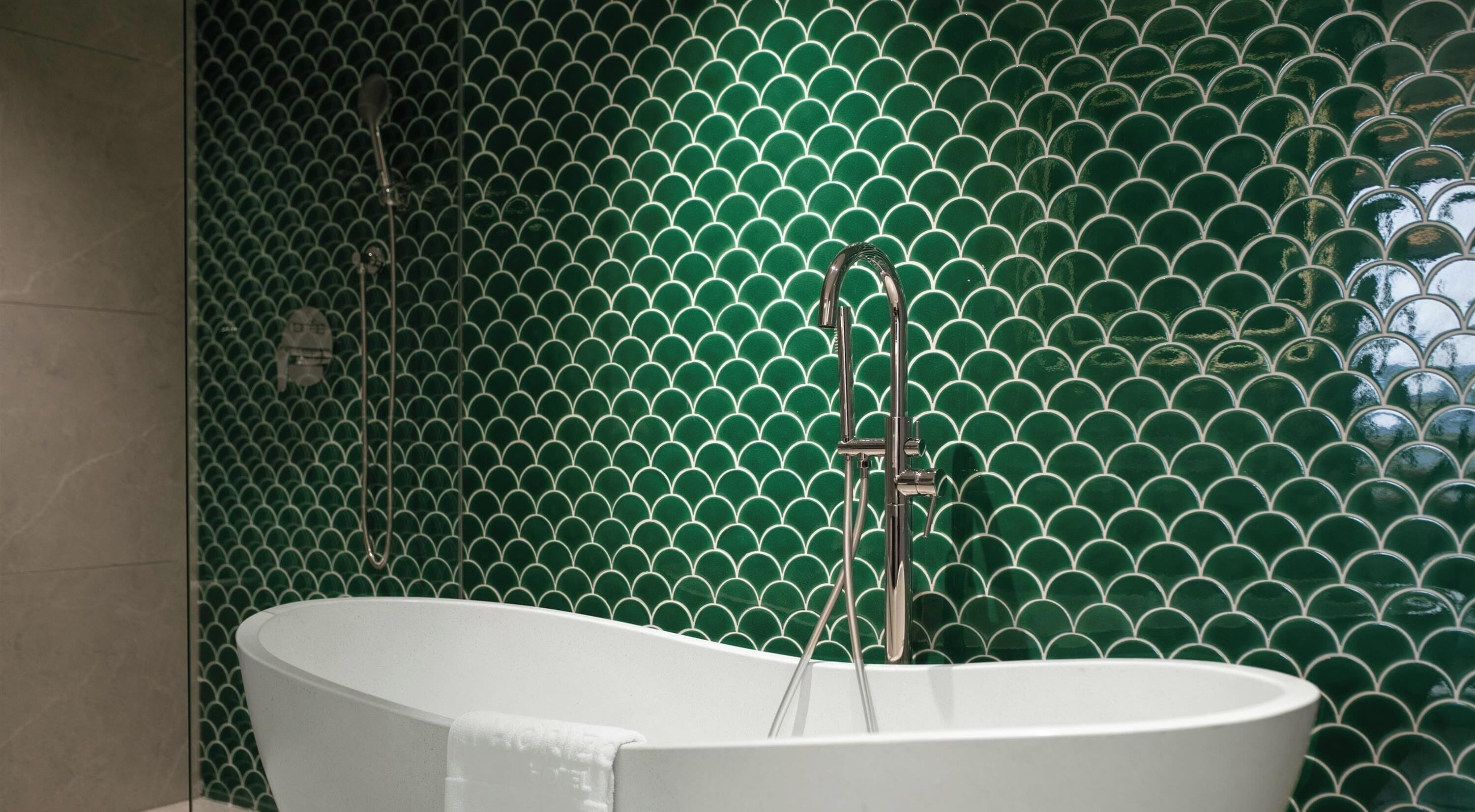 A bathtub in a bathroom with a green tiled wall.
