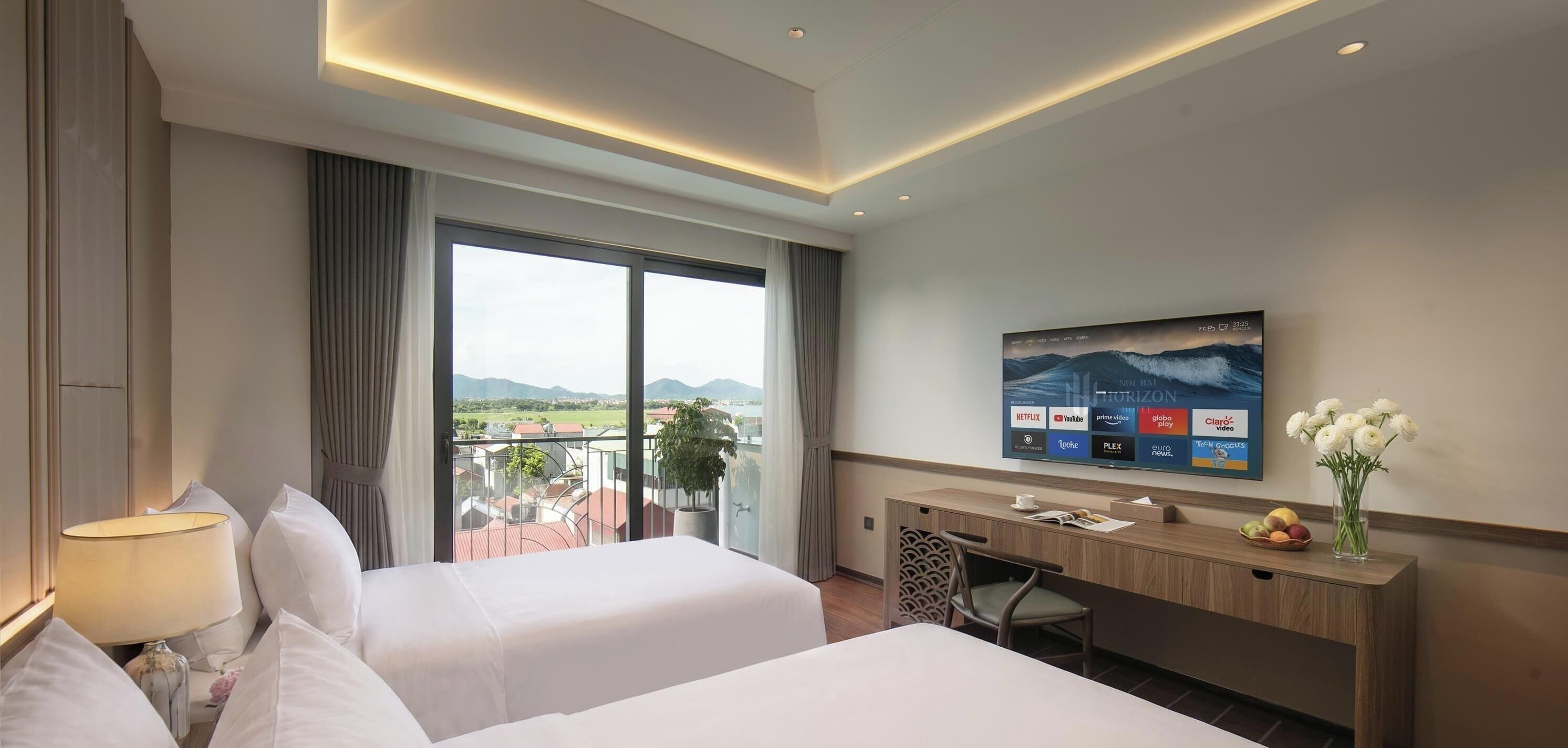 A hotel room with two beds, a desk, a television, and a view of the mountains.