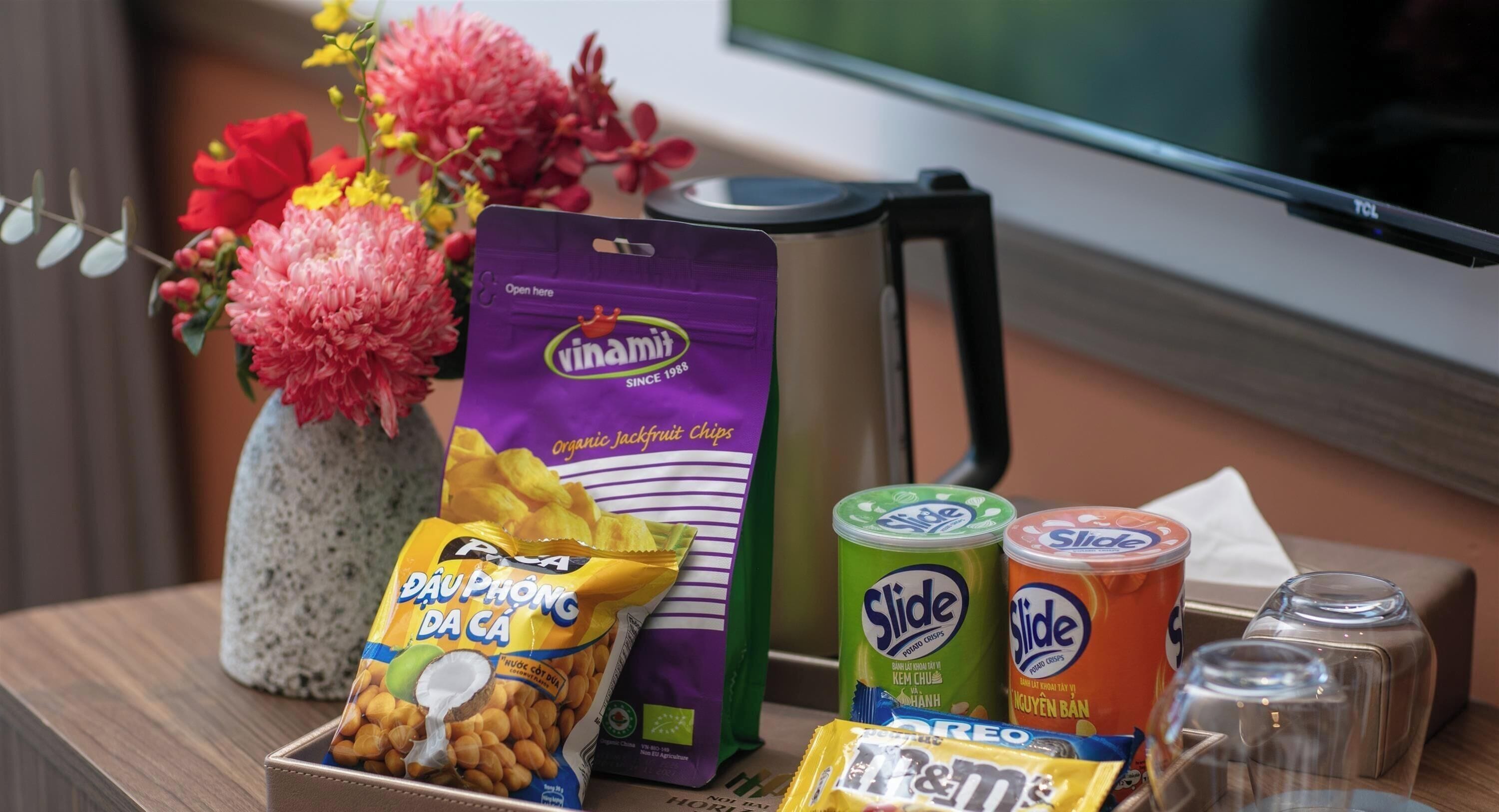 A table with snacks, a coffee maker, and a vase with flowers.