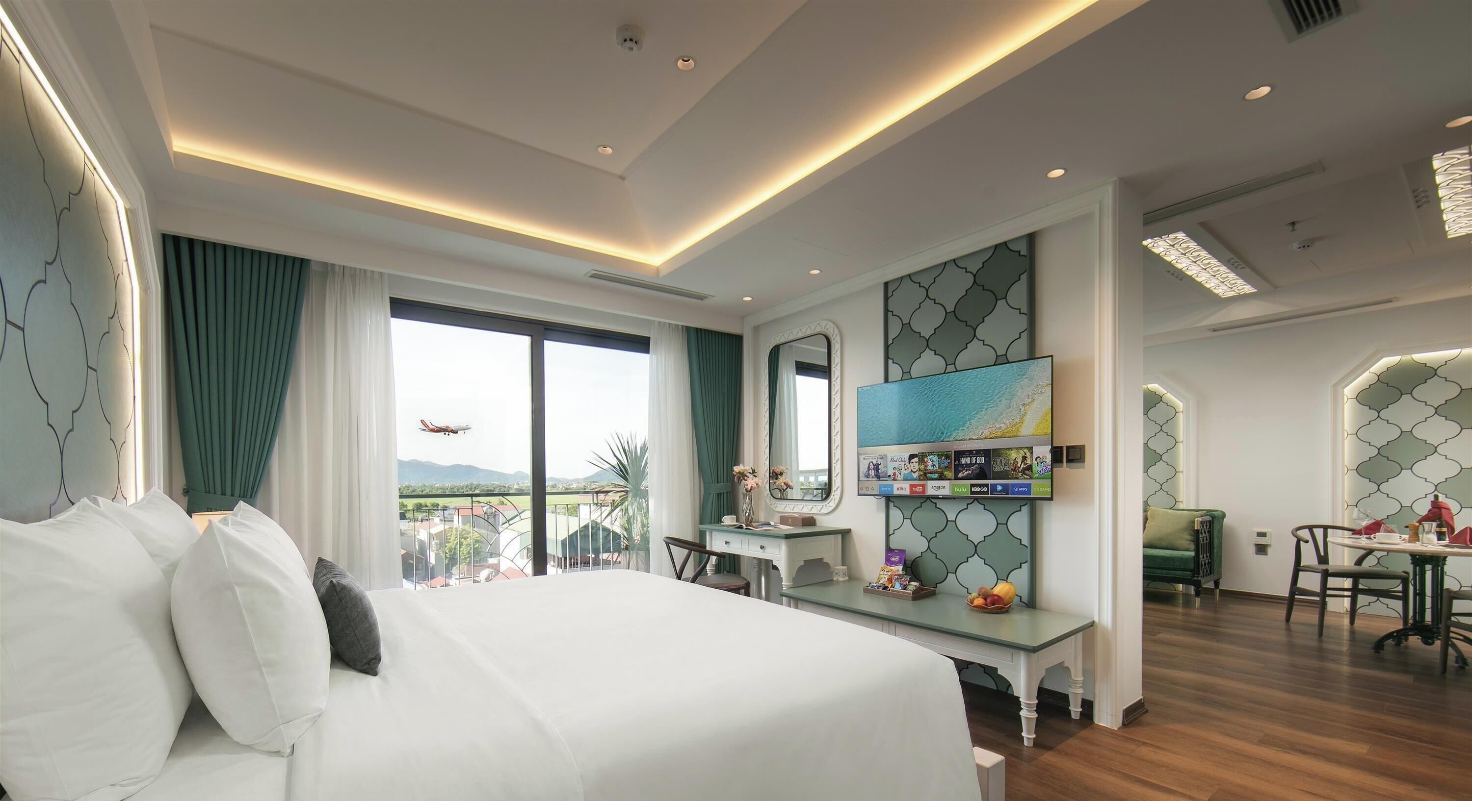 A hotel room with a large bed, a desk, a TV, and a balcony with a view of the mountains.