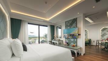 A hotel room with a large bed, a desk, a TV, and a balcony with a view of the mountains.